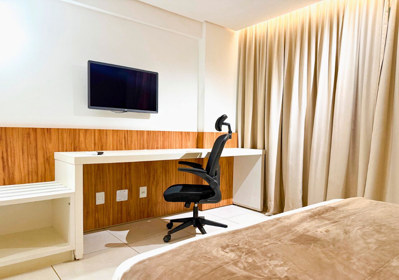 A hotel room with a bed, a desk with a chair, a television, and a curtain.