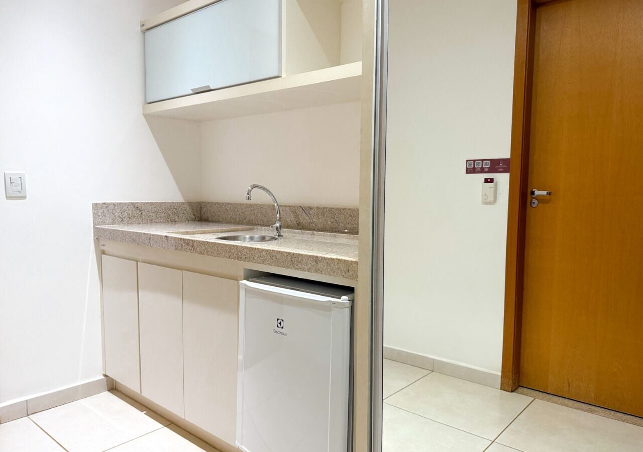 A compact kitchen with a built-in sink, a small refrigerator, and a wooden door.