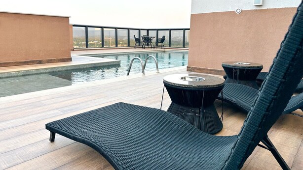Un espace piscine aménagé sur le toit, avec des chaises longues et une table, le tout entouré d’une balustrade en verre.