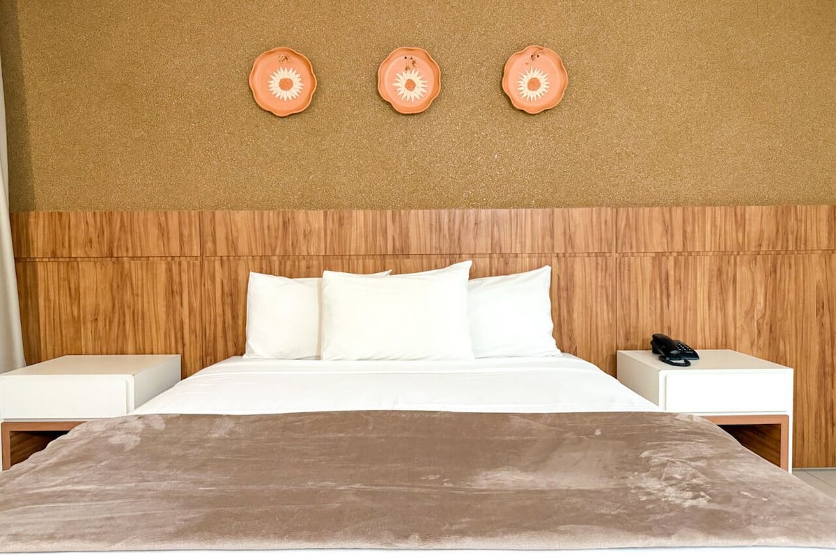 Een bed met witte lakens, een houten hoofdbord en een bruine plaid.