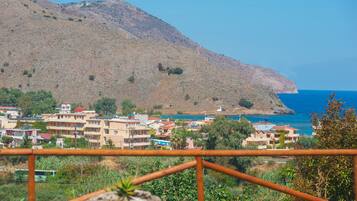 A coastal town with buildings on a hillside, a clear view of the sea, and a metal railing in the foreground.