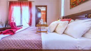 A hotel room with two beds, a wooden headboard, a bedside table with a lamp, and a window with red curtains.