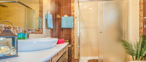 A modern bathroom with a glass shower enclosure, a large sink, and a mirror.