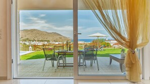 Ein Zimmer mit einer Schiebetür, die auf eine Terrasse mit Tisch und Stühlen führt, mit Blick auf eine Berglandschaft und einen Poolbereich.