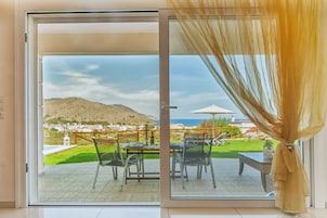 Una habitación con puerta corrediza de vidrio que da a un patio exterior con mesa y sillas, vistas a un paisaje montañoso y una zona de piscina.