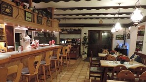 A restaurant with a bar area, wooden chairs, and tables.
