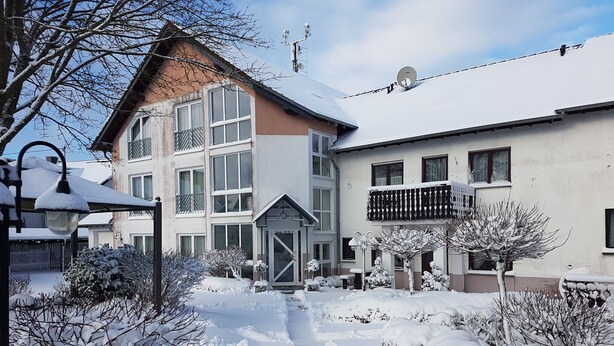A snow-covered residential area with a two-story building, a balcony, and a pathway.