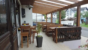 An outdoor seating area with wooden tables and benches, a potted plant, and a sign for a restaurant.