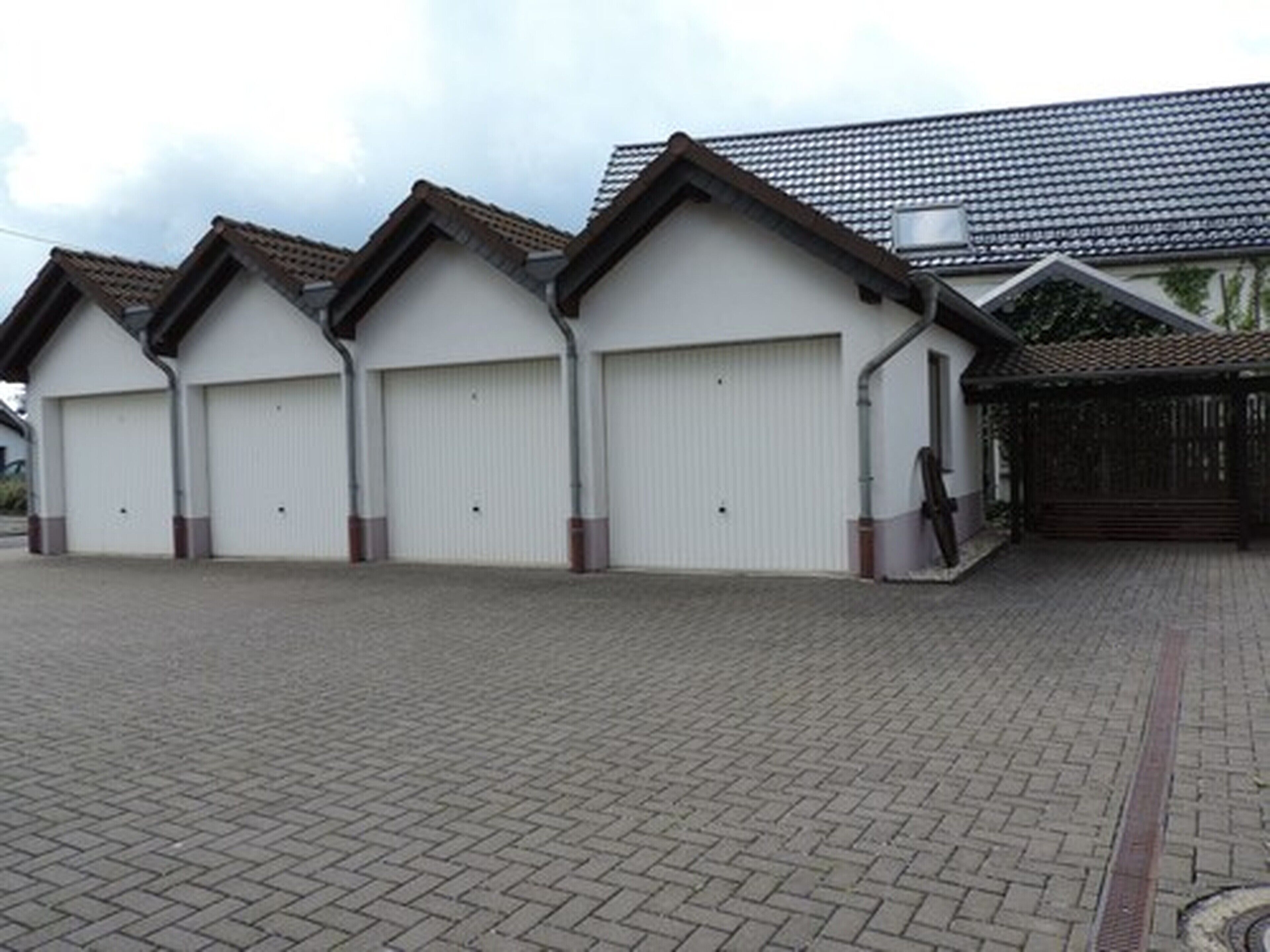 Ein Gebäude mit drei großen weißen Garagentoren, einem Ziegeldach und einer gepflasterten Auffahrt.