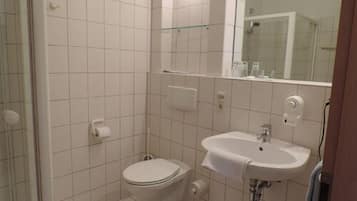 A small, clean bathroom with white tiles, a toilet, a sink, and a glass shower enclosure.