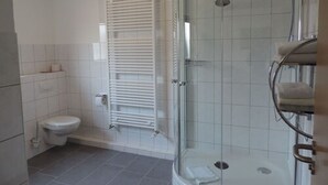 A modern bathroom with a glass-enclosed shower, a toilet, and a towel rack.