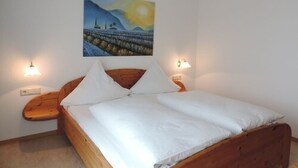A bedroom with a wooden bed, white bedding, two bedside tables with lamps, and a painting of a landscape on the wall.