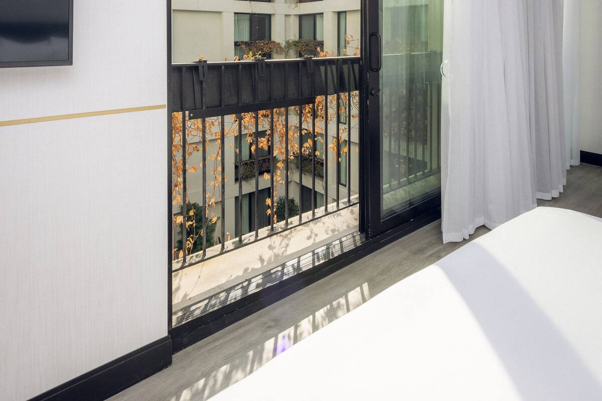Ein modernes Hotelzimmer mit einer großen Schiebeglasdoor zum Balkon mit Blick auf andere Gebäude und einen Garten.