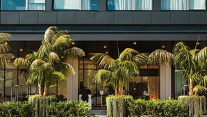 A modern building with large windows and a well-maintained outdoor area with palm trees and greenery. - The Godfrey Hotel Hollywood (Los Angeles)