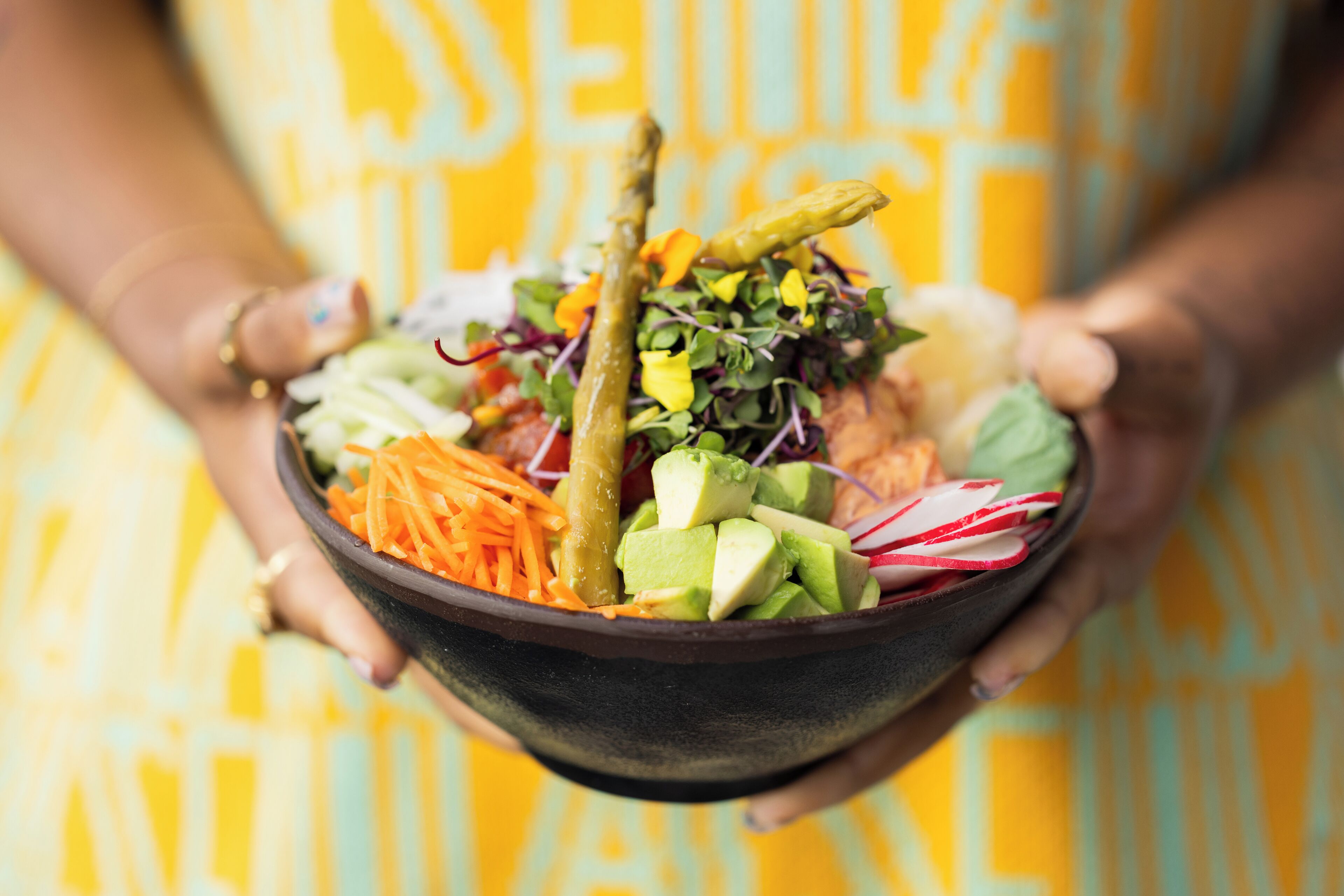 Un bol de salade contenant divers légumes et un morceau de viande, tenu par une personne portant une robe à motifs.