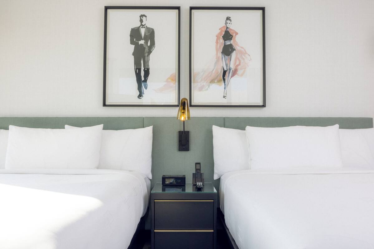 Ein Hotelzimmer mit zwei Betten, einem Nachttisch mit Telefon und zwei gerahmten Bildern an der Wand.