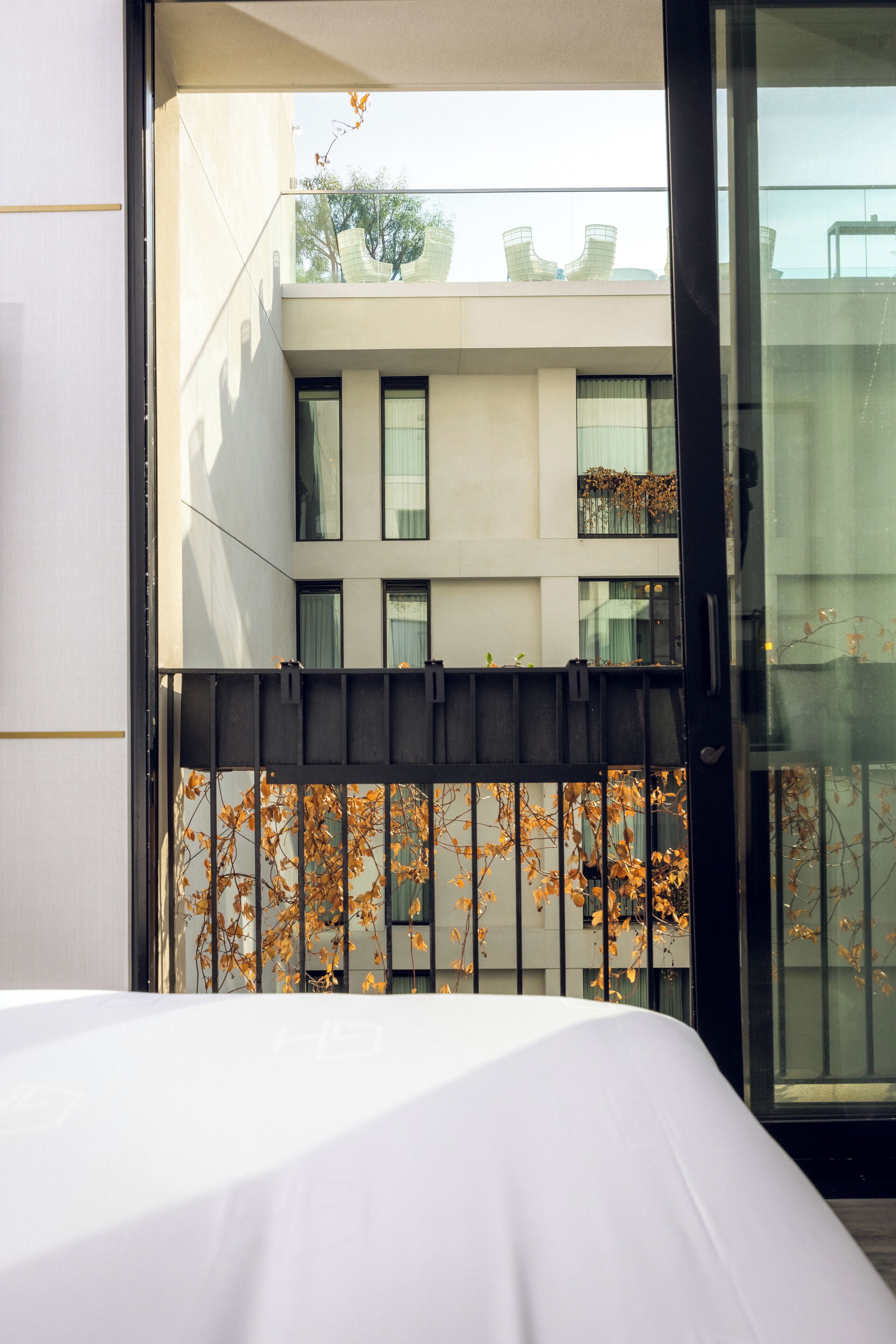 A hotel room with a balcony, a bed, and a view of a building with multiple windows and a balcony.