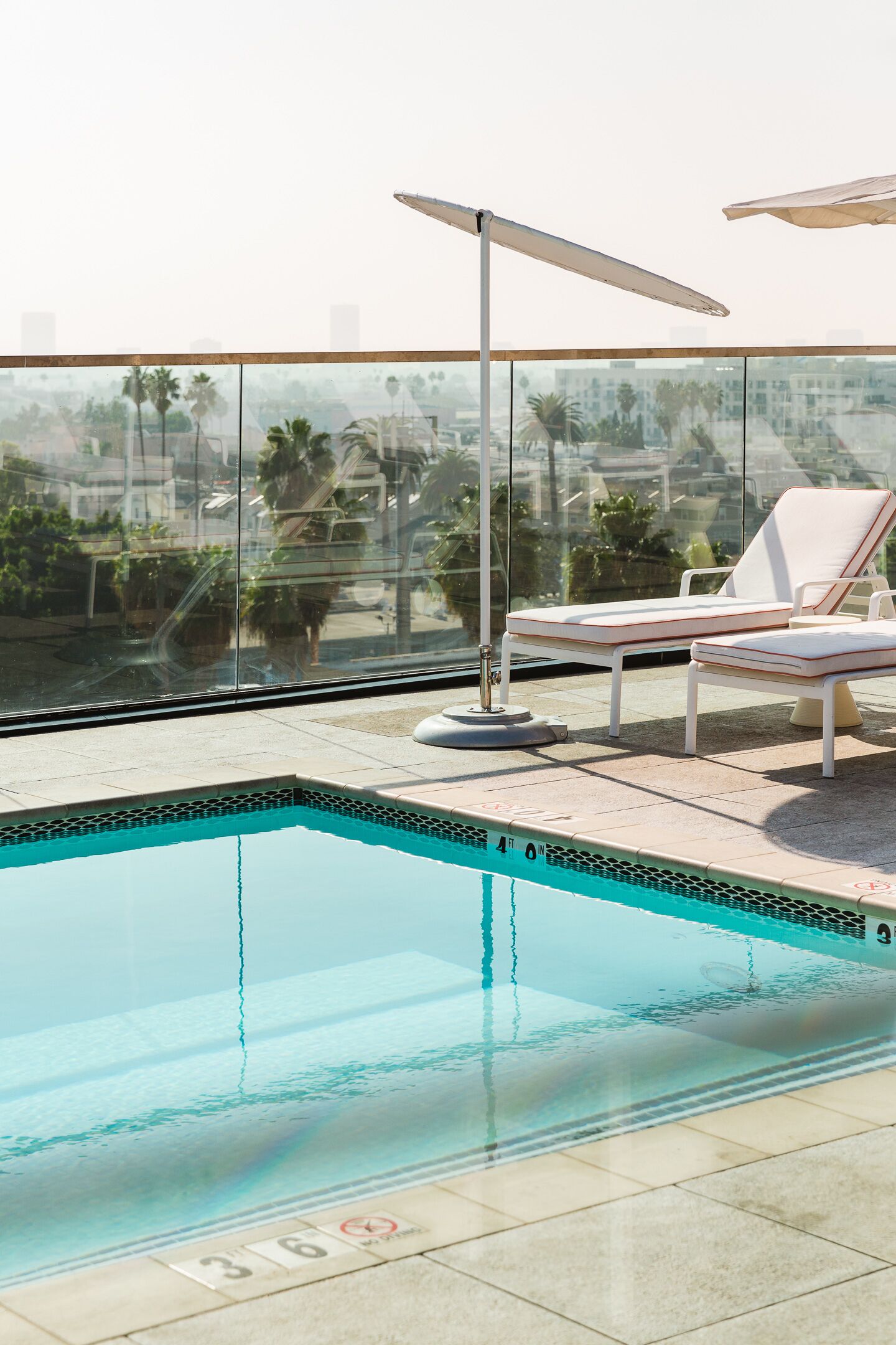 A rooftop pool with lounge chairs and a glass balustrade overlooking a cityscape.