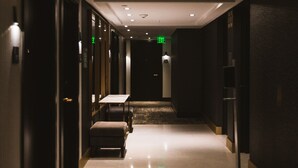 A hotel corridor with a carpeted floor, a bench, and a table.