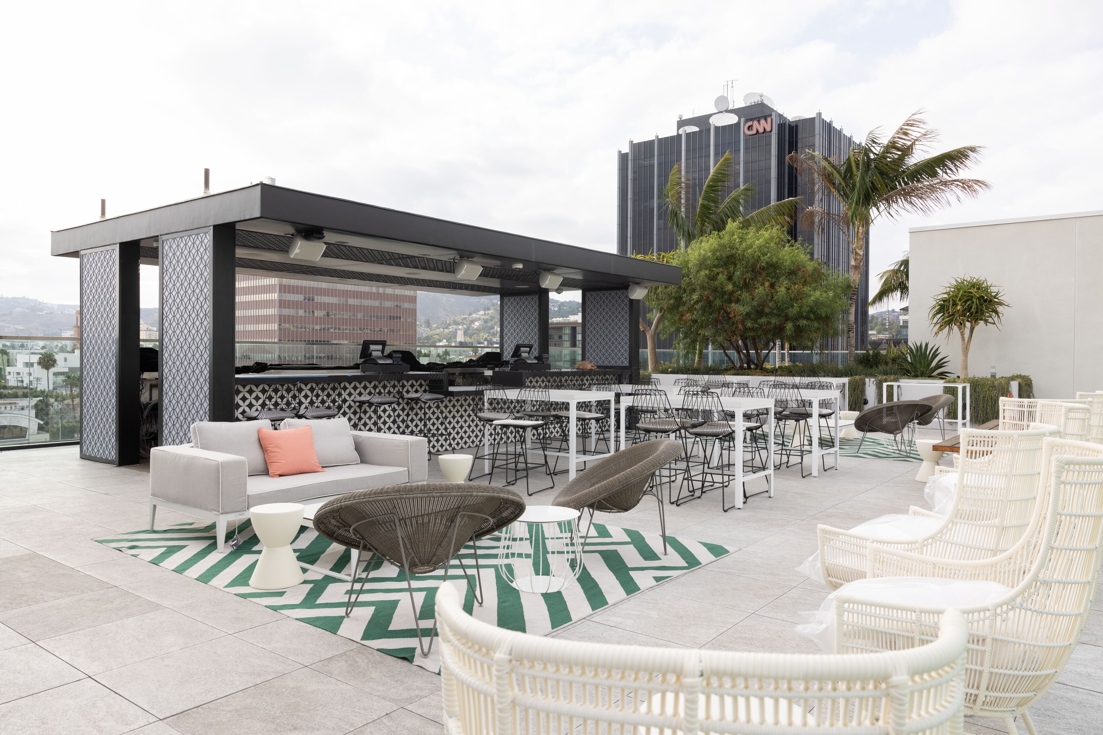 Eine Dachterrasse mit Außenbereich, darunter weiße Korbstühle und eine Couch, mit Blick auf die Stadt.