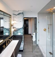 Een moderne badkamer met een marmeren wand, een douchecabine van glas en een grote spiegel.
