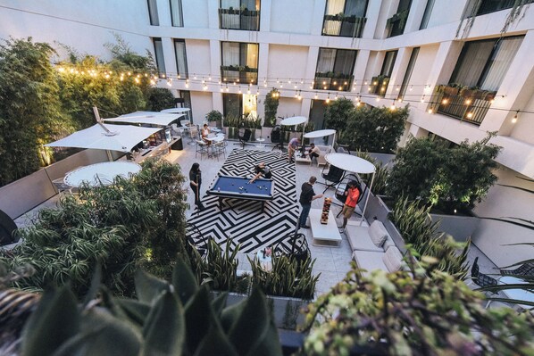 A rooftop patio with a pool table, outdoor seating, string lights, and potted plants. - The Godfrey Hotel Hollywood (Los Angeles)