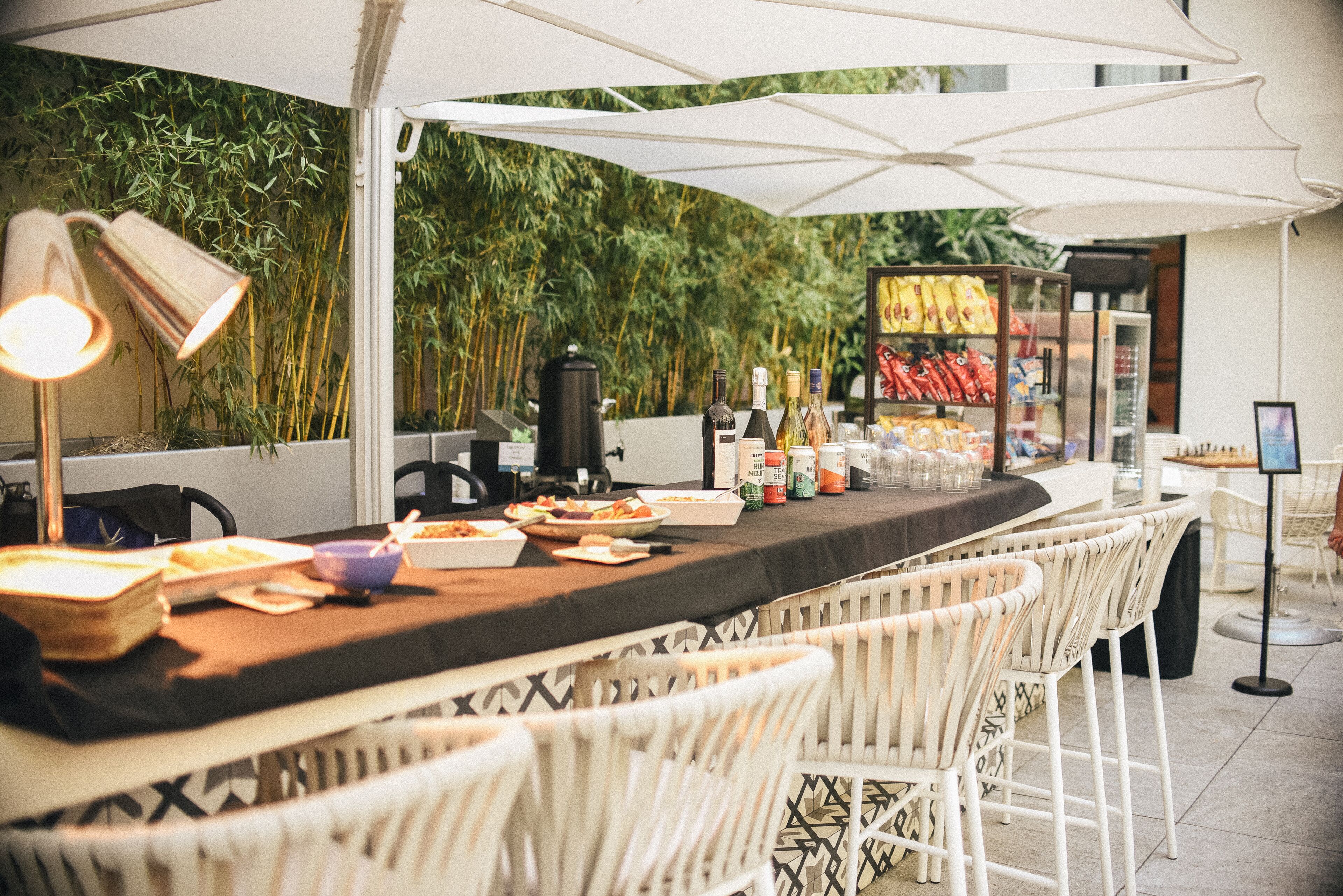 Un área de bar al aire libre con una barra larga, sillas de mimbre blanco y un fondo de bambú.
