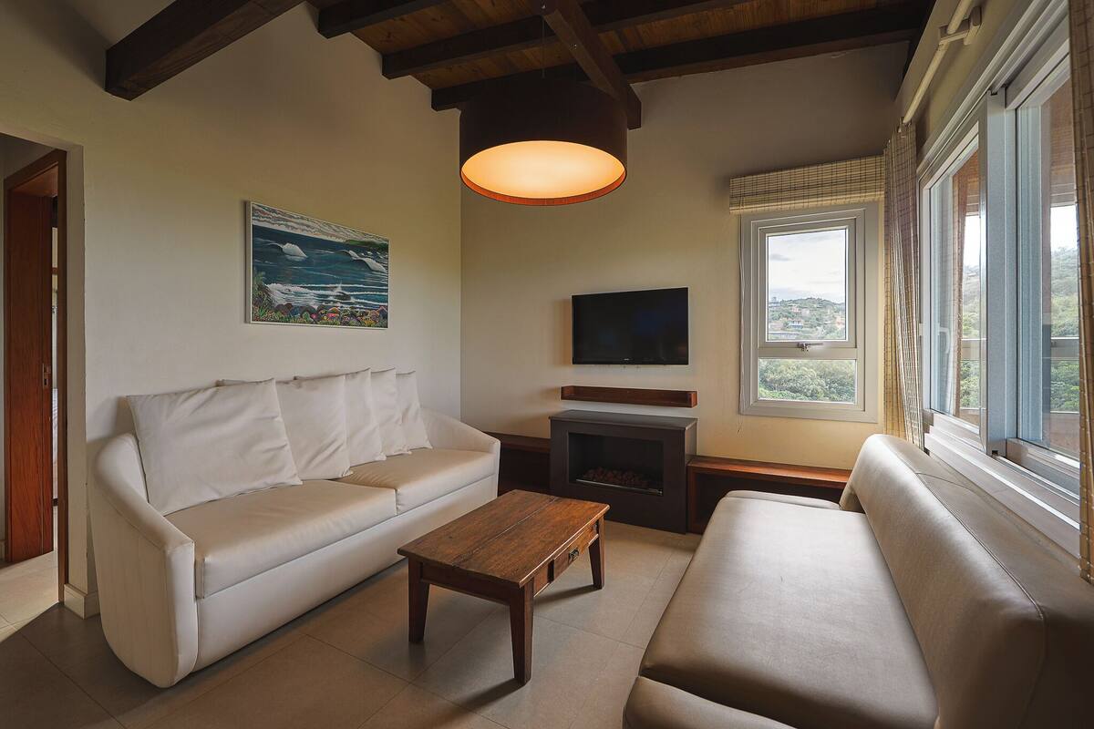 A living room with a sofa, a coffee table, a fireplace, a TV, and a window with curtains.
