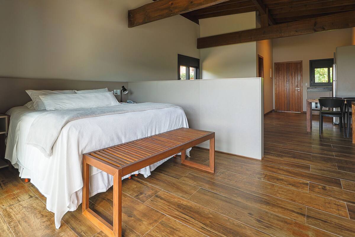 A bedroom with a wooden bed, a bench, and a desk area with chairs.