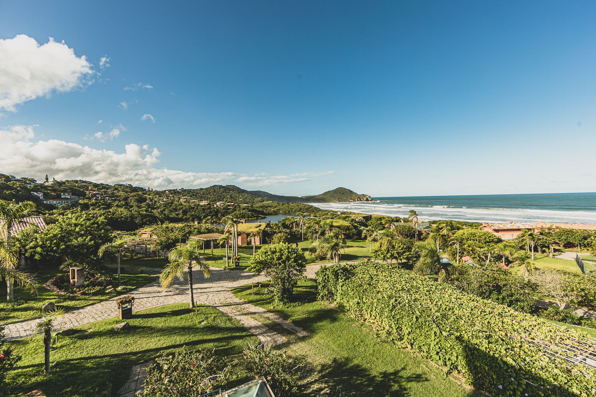 A coastal landscape with a paved pathway, lush greenery, and a beach.