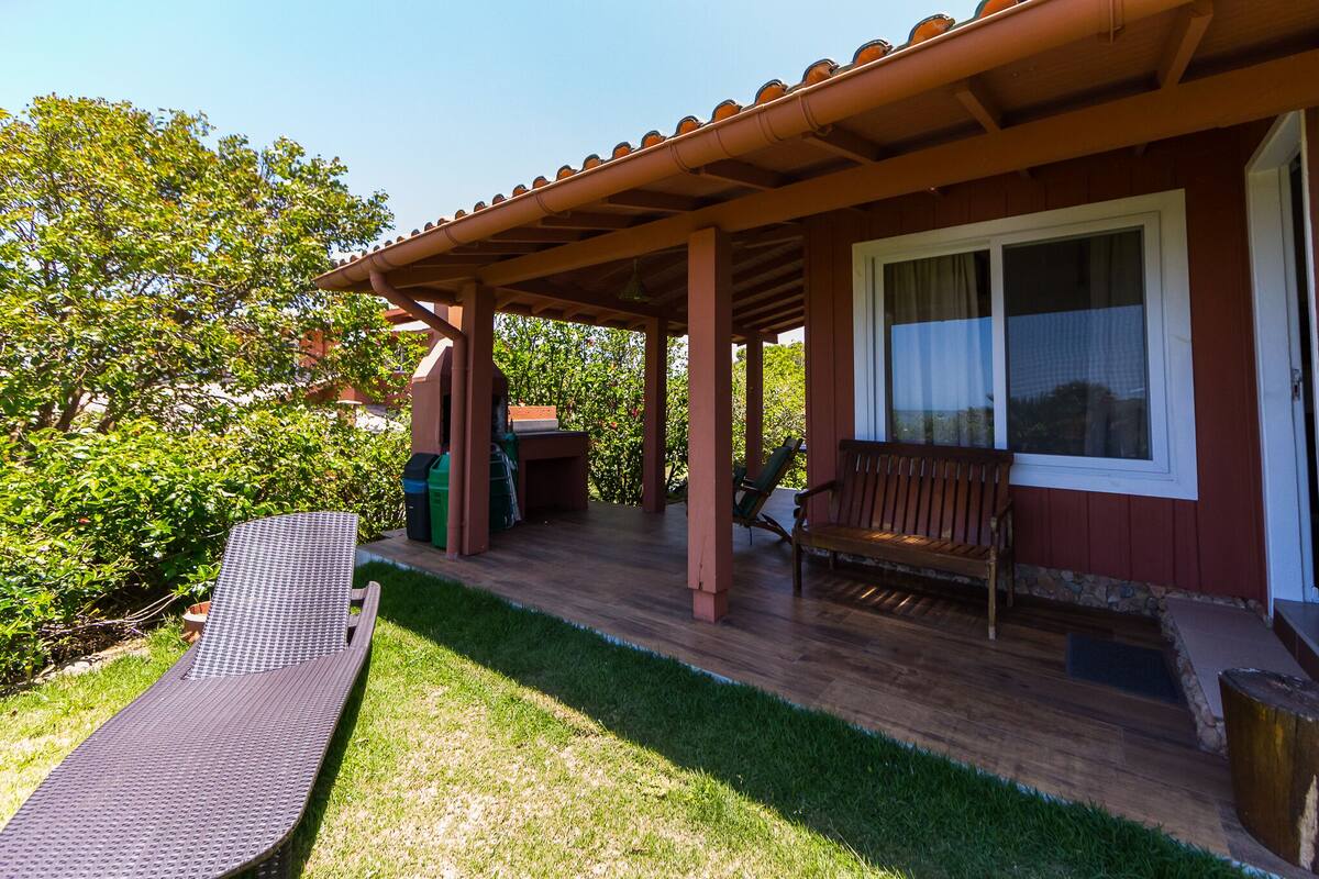 A covered outdoor area with a wooden deck, a lounge chair, and a bench.