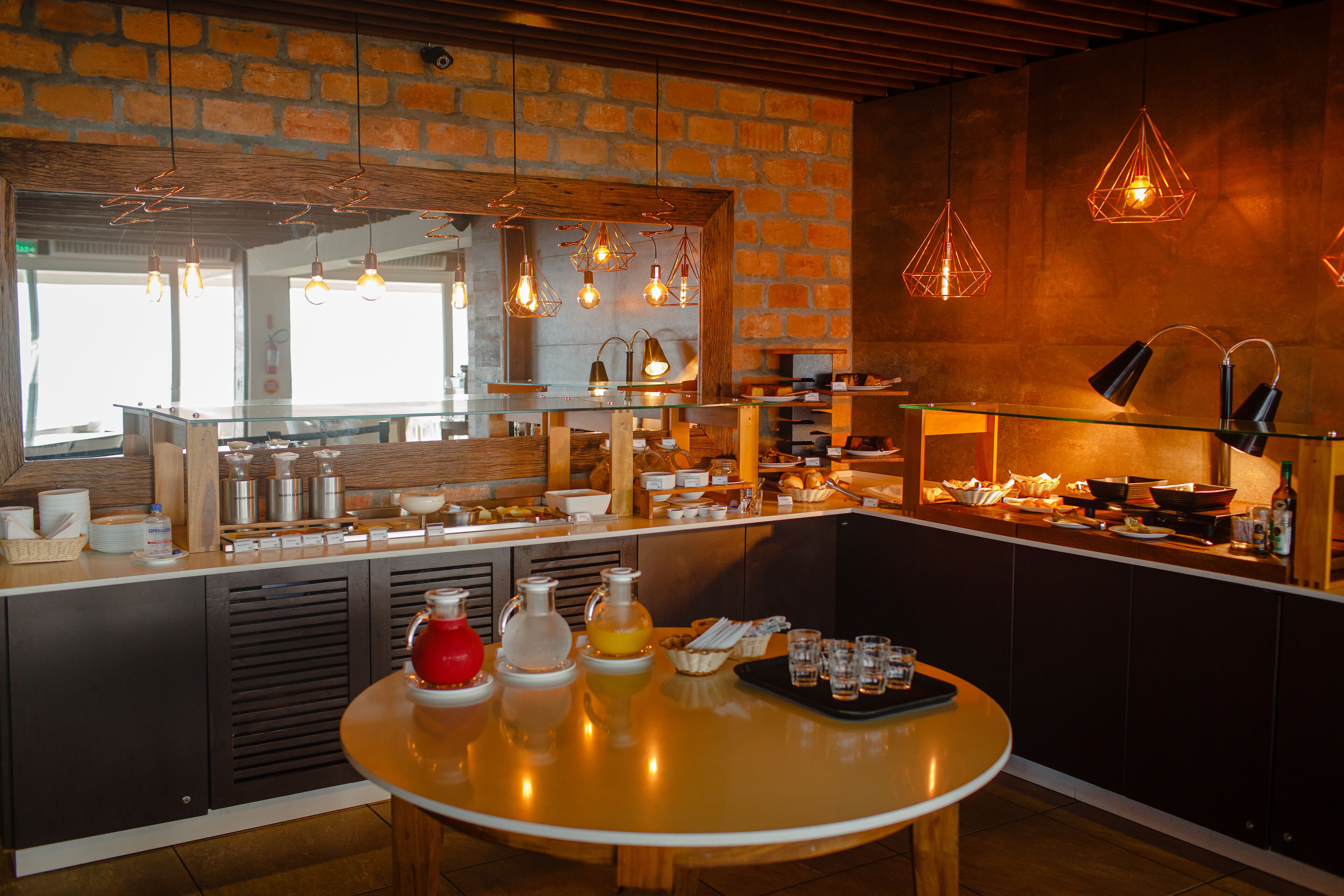 A breakfast bar with a brick wall, hanging pendant lights, and a variety of breakfast items.