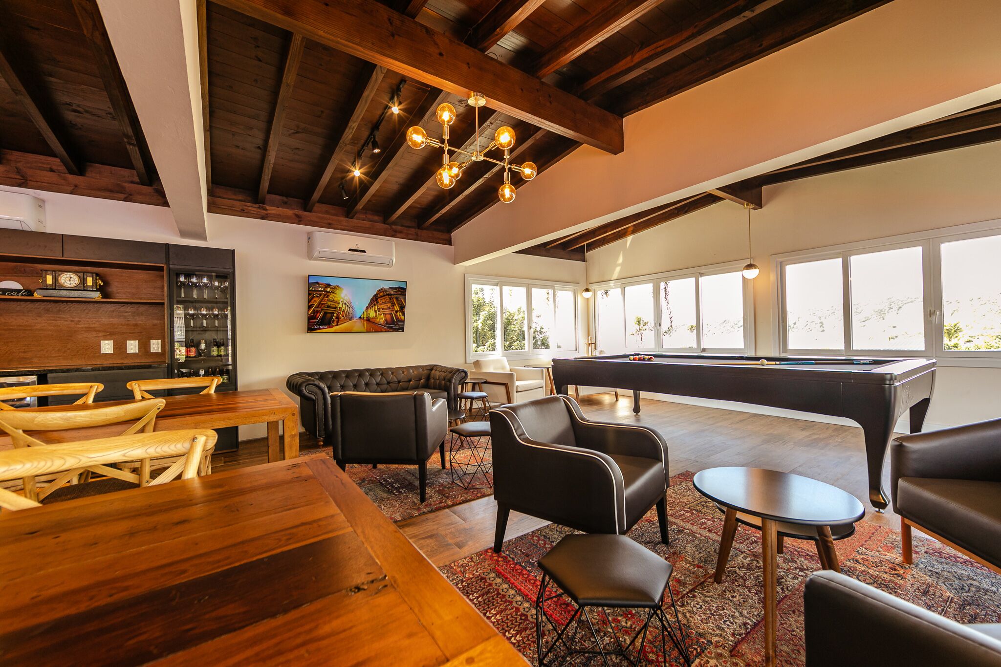 A spacious lounge area with a pool table, comfortable seating, and a bar area with a clock and bottles.