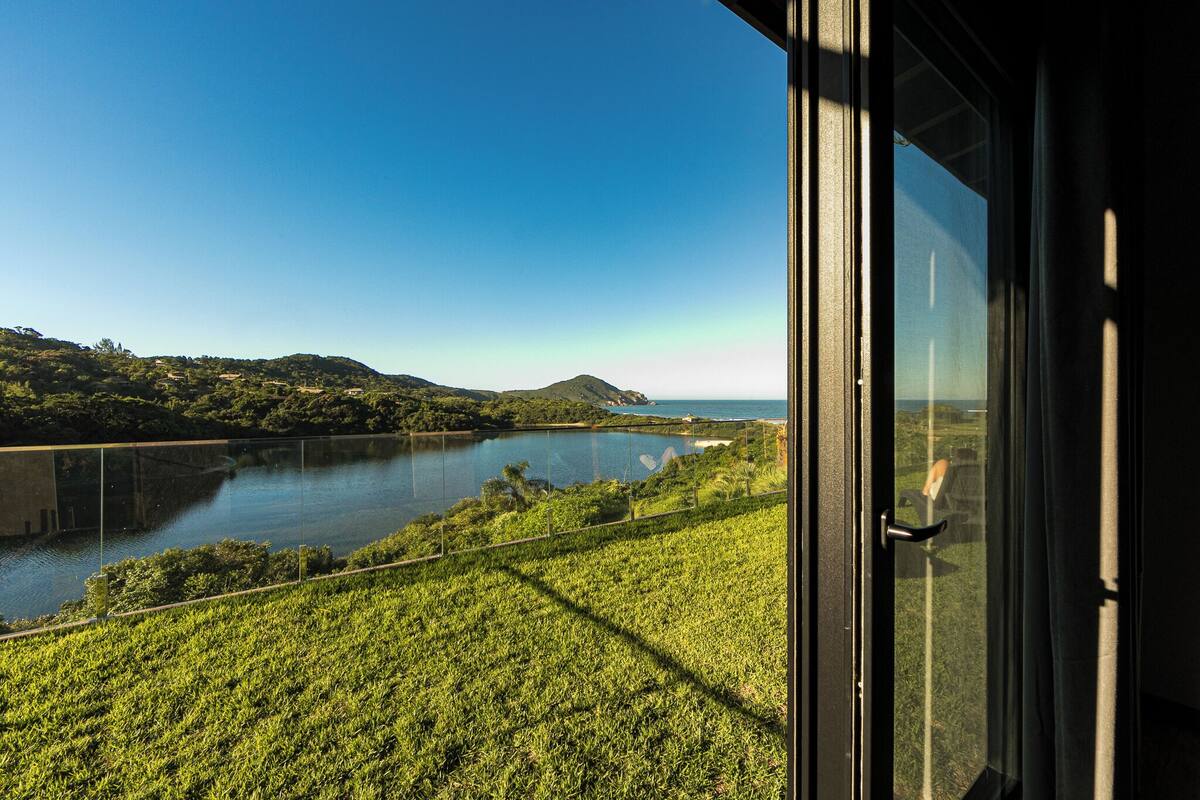 A view from a window overlooking a lake, surrounded by greenery and hills.