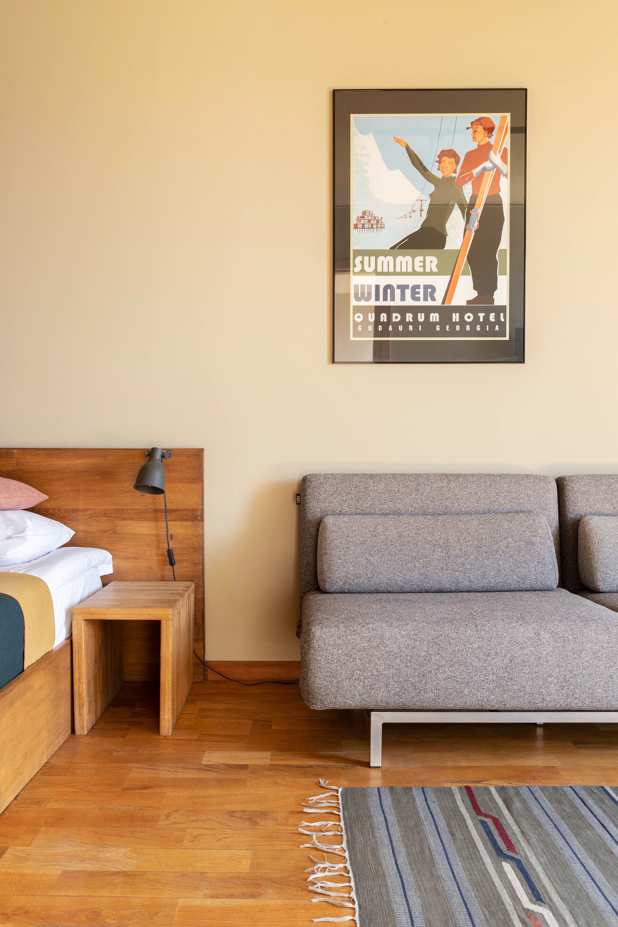 Ein Schlafzimmer mit einem Holz-Kopfteil, einem Bett mit Kissen, einem Nachttisch, einem grauen Sofa und einem gerahmten Poster an der Wand.
