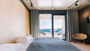 A hotel room with a bed, a chair, a TV, and a view of mountains. - Quadrum Ski & Yoga Resort (Kazbegi)