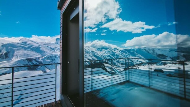 A balcony with a glass railing overlooking a snowy mountain landscape. - Quadrum Ski & Yoga Resort (Kazbegi)