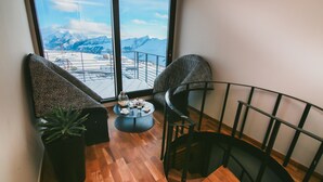 A balcony with a view of snow-covered mountains, a small table with a drink, and two patterned chairs. - Quadrum Ski & Yoga Resort (Kazbegi)