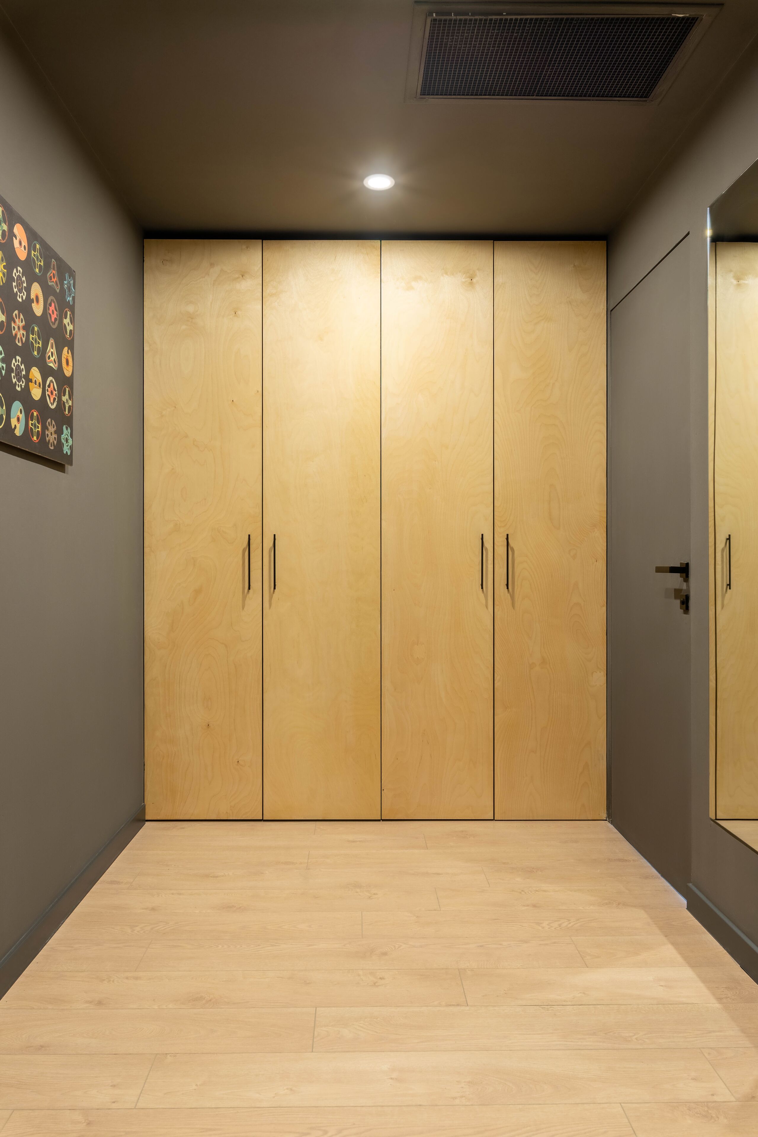 A room with a large wooden wardrobe, a grey wall, and a wooden floor.
