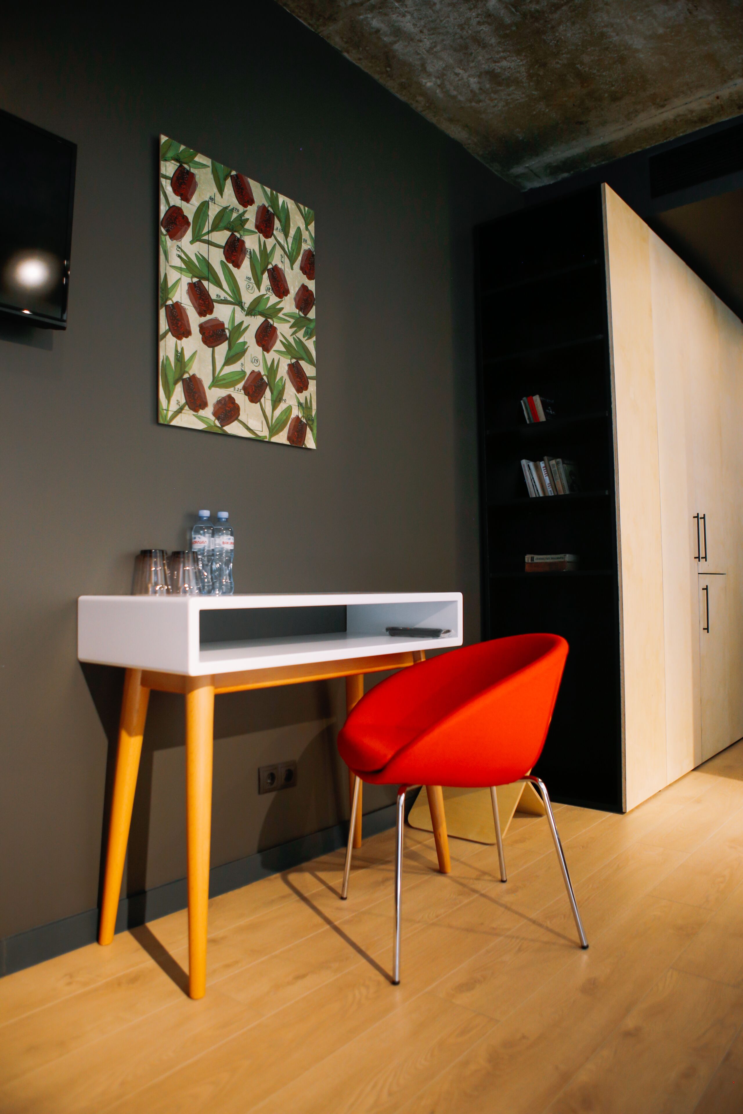 A modern room with a white desk, a red chair, a bookshelf, and a wall-mounted TV.