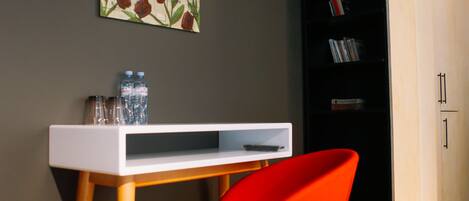 A modern room with a white desk, a red chair, a bookshelf, and a wall-mounted TV.