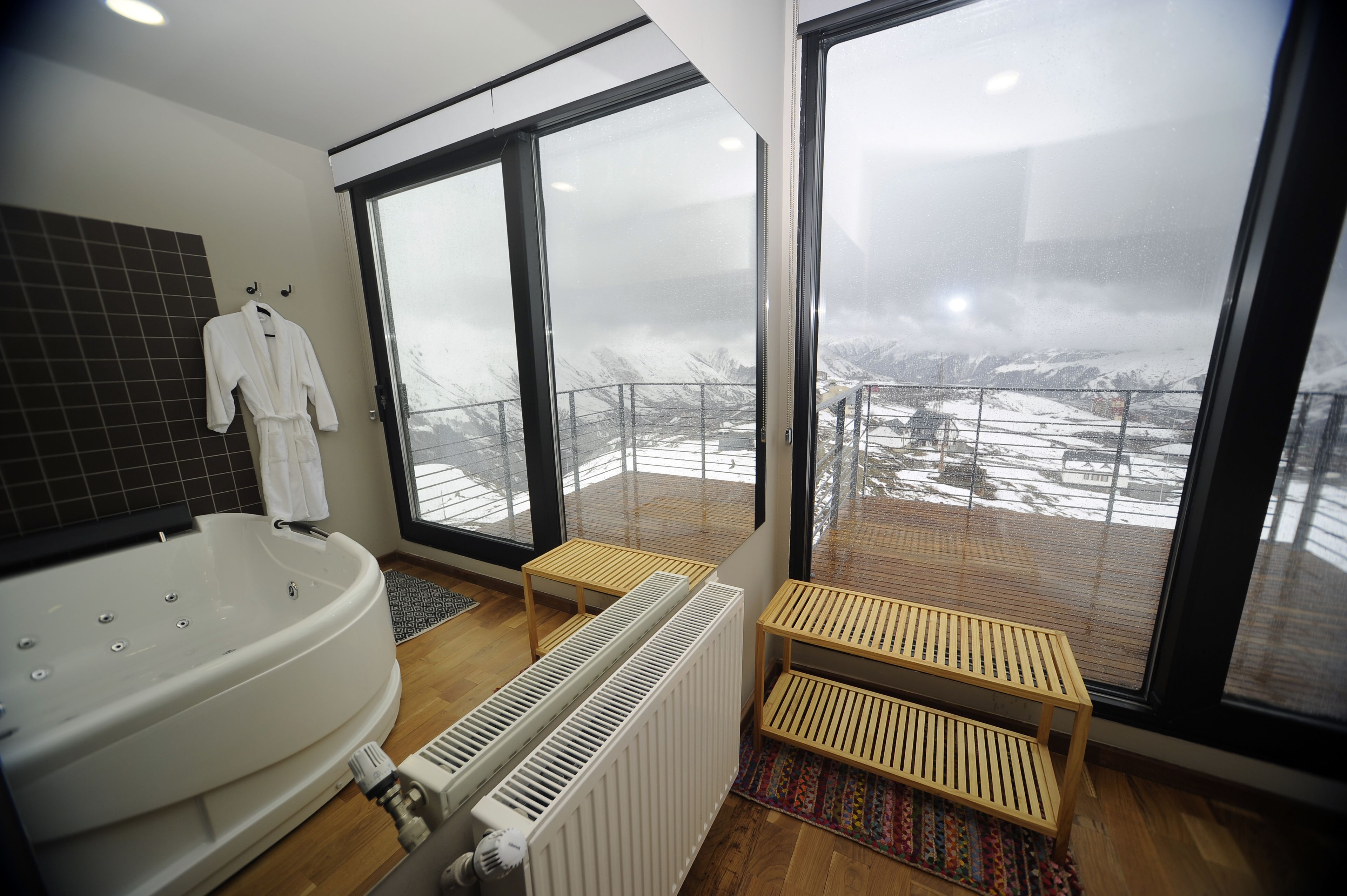 Et moderne badeværelse med et stort badekar, en hvid radiator og udsigt til et snedækket landskab gennem store skydedøre.