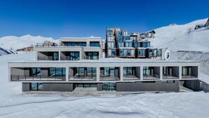 A modern multi-story hotel with large windows and balconies, situated in a snowy mountainous area. - Quadrum Ski & Yoga Resort (Kazbegi)