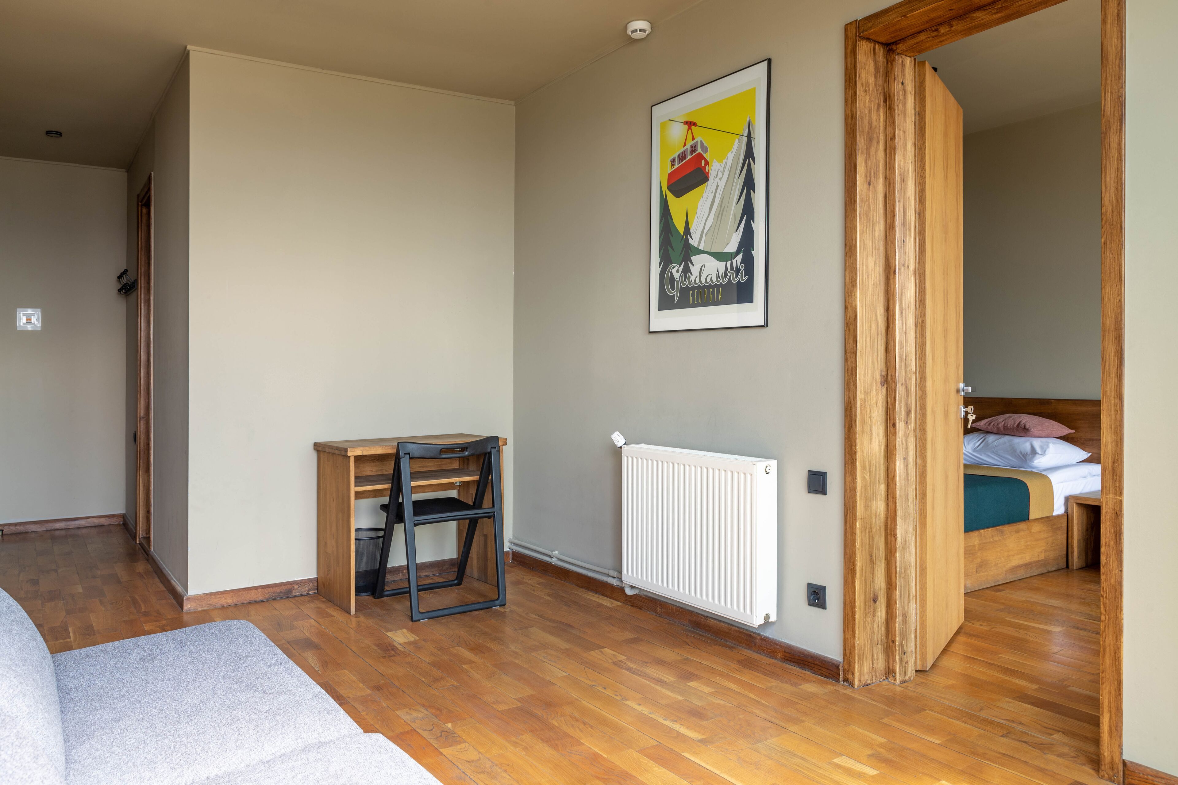 Ein Zimmer mit Holzboden, einem Bett mit Kopfteil, einem Heizkörper und einem gerahmten Bild an der Wand.