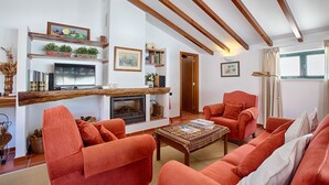 Una sala de estar con chimenea, vigas de madera, sofás naranja y televisor.