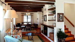 Una sala de estar con chimenea, un sofá, una mesa de comedor con sillas y una escalera.