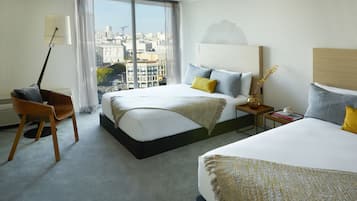 Ein Hotelzimmer mit zwei Betten, einem Schreibtisch, einem Stuhl und Blick auf die Stadt.