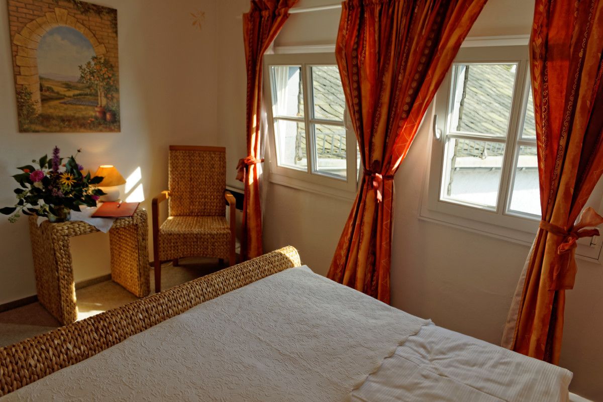 A room with a bed, a chair, a table with a lamp, and a window with curtains.