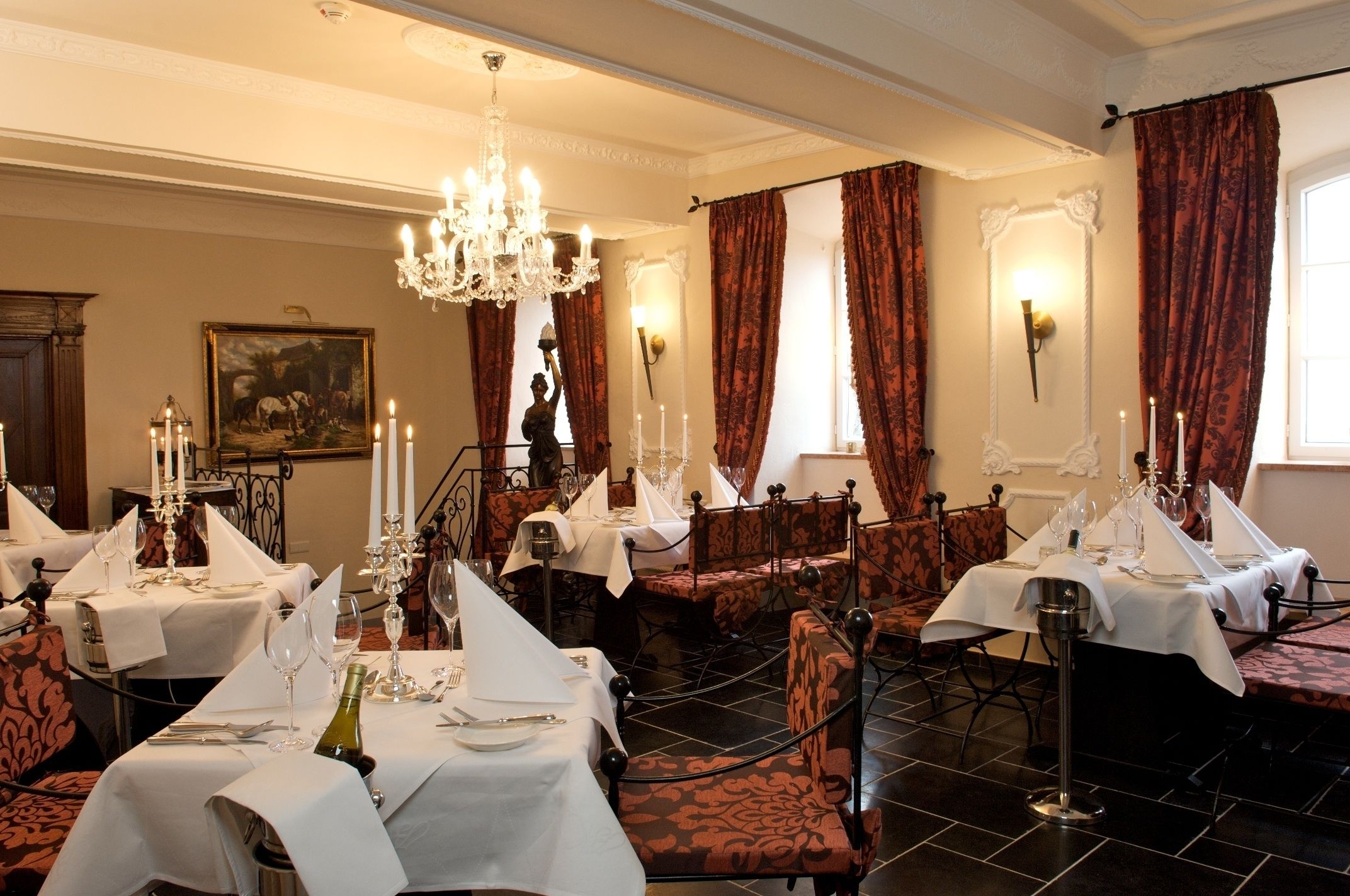 A formal dining room with multiple tables set for service, a chandelier, and red curtains.