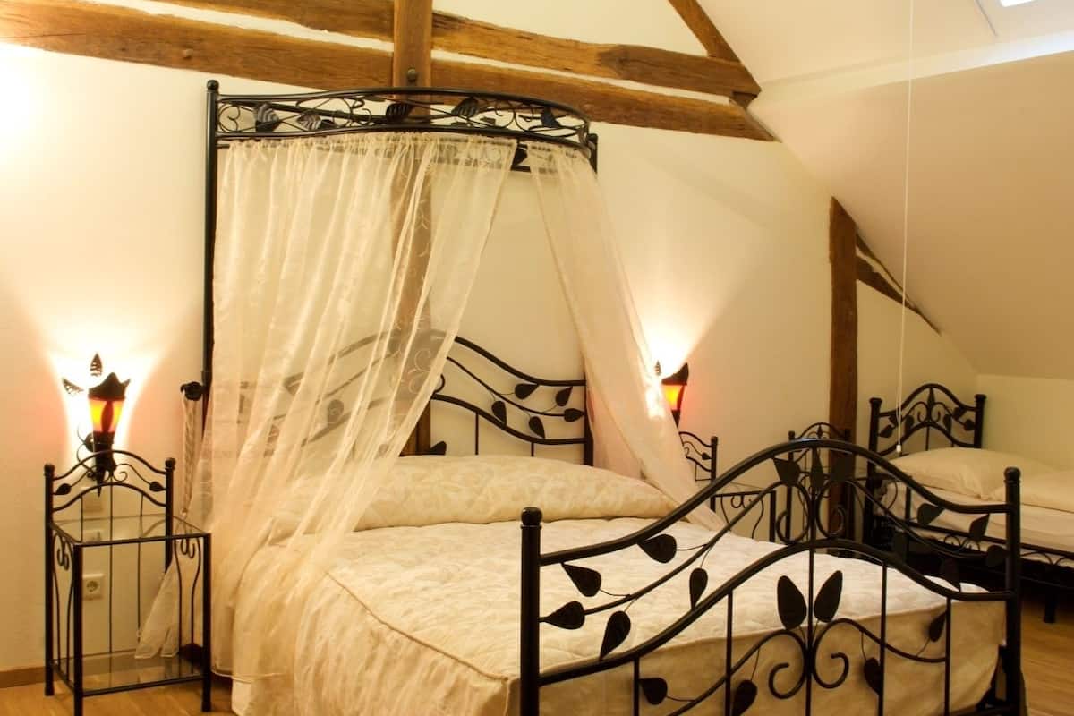 A bedroom with a four-poster canopy bed, wooden beams, and a sloped ceiling.